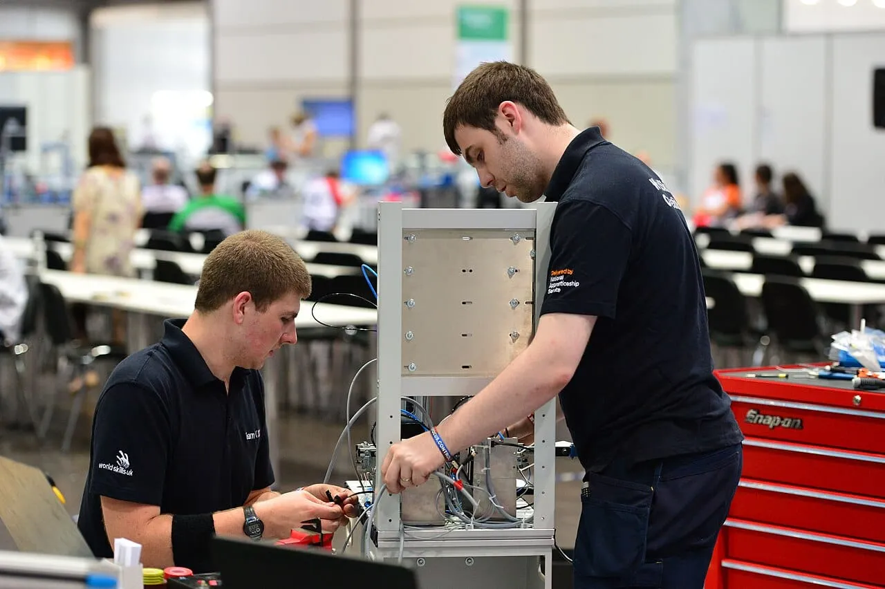 Two young competitors connecting wires on a machine at a skills competition