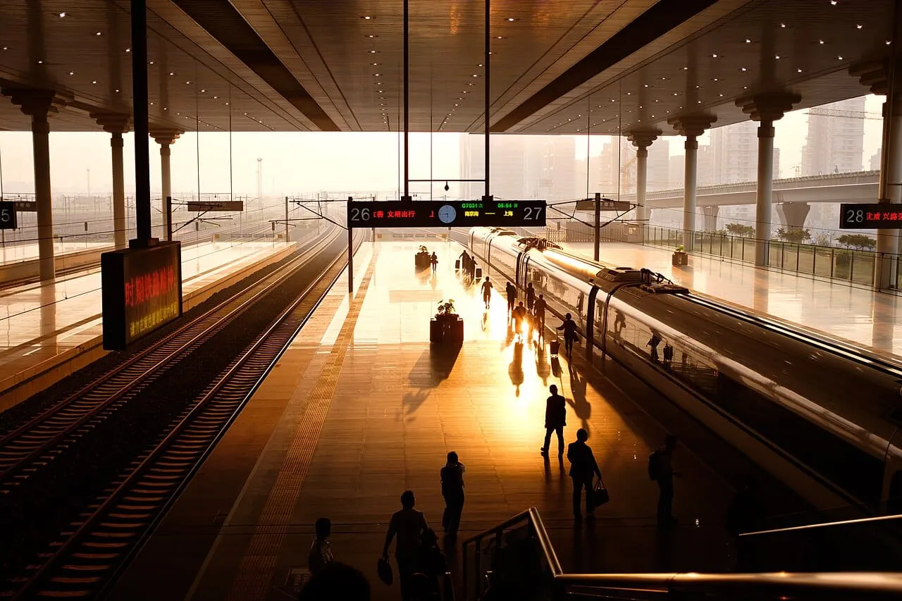 Passengers walking beside a high-speed train on a platform at sunrise