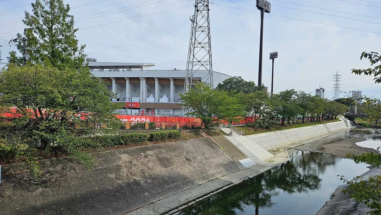 The Mizuho Athletic Stadium in Nagoya with red Asian Games banners, seen across a small river