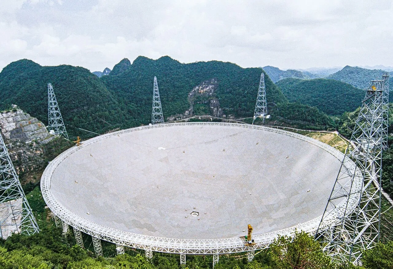 A huge round white radio telescope dish among green mountains