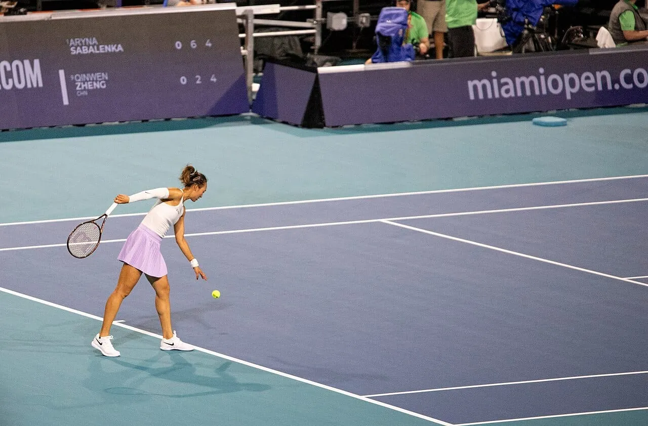 Tennis player Zheng Qinwen bouncing a ball before serving on a blue court