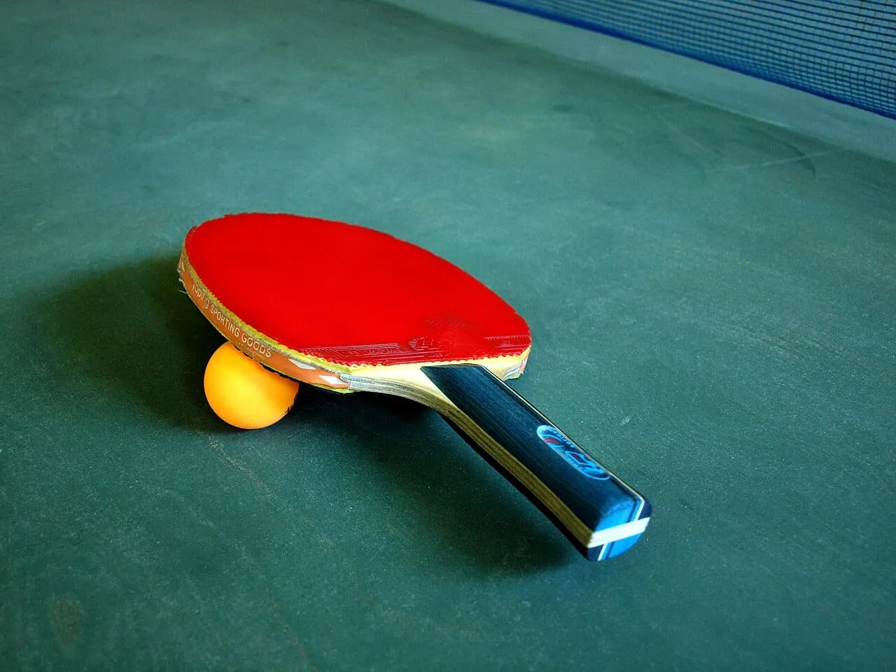 A red table tennis bat and an orange ball on a green table